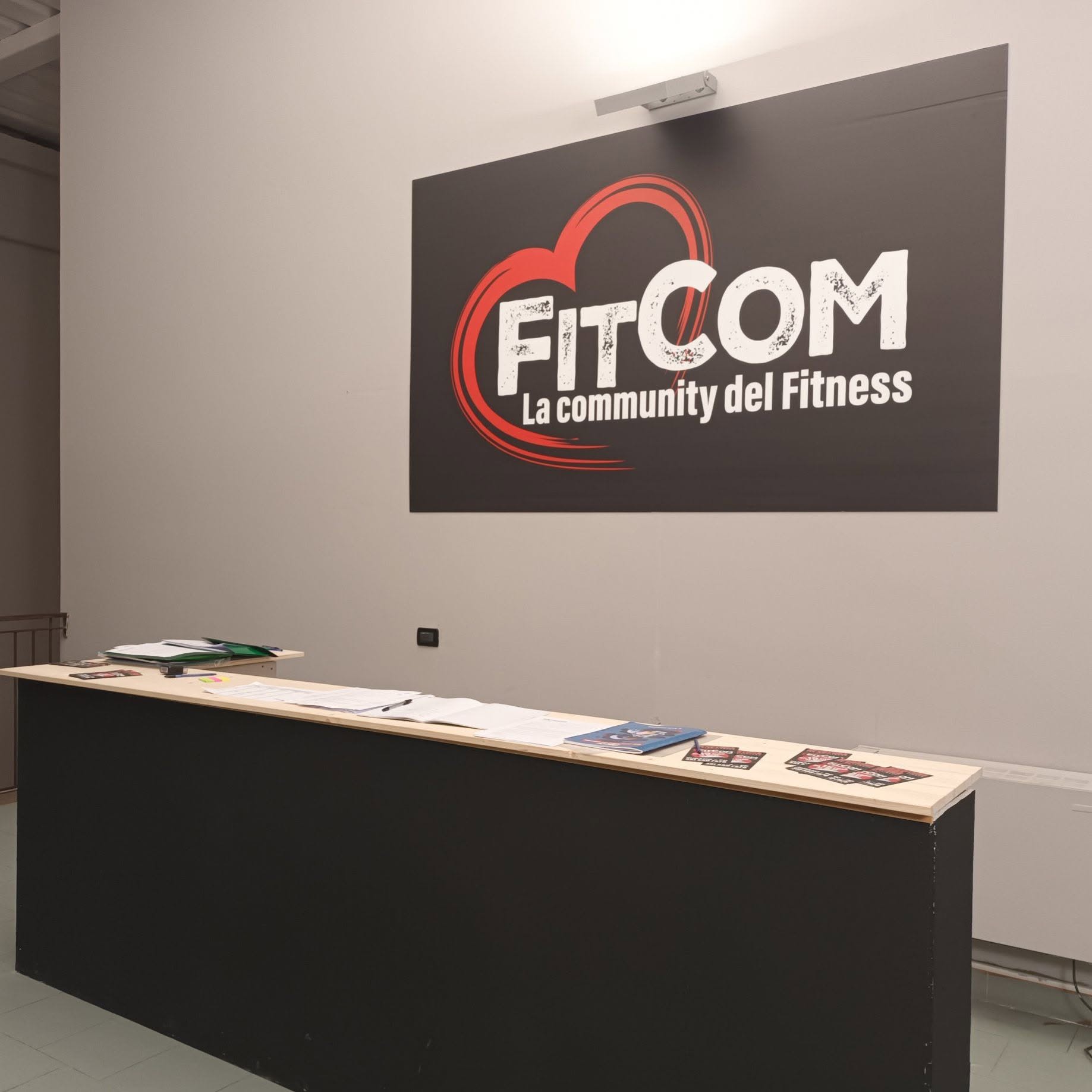 A reception desk with papers and brochures sits beneath a large wall logo in a softly lit interior.