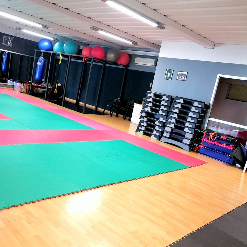 Empty indoor training room with colorful floor mats, exercise balls, hanging bags and stacked equipment.